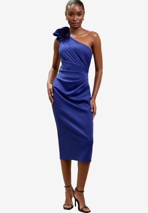 Robe asymétrique en bleu profond avec un détail de fleur texturé à l'épaule, tissu drapé et longueur midi ajustée.