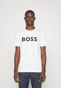 T-shirt blanc à manches courtes en coton, avec un grand graphisme « BOSS » noir sur le devant. Col rond, coupe décontractée.