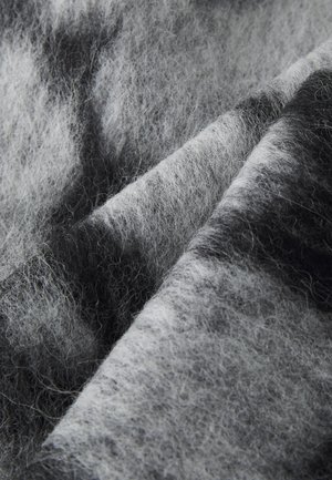 Grau- und schwarzer Wollstoff mit einer weichen, flauschigen Textur, die in geschichteten Falten angeordnet ist, und einem Farbverlauf aus helleren und dunkleren Fasern.