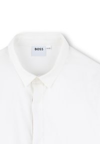 Camicia bianca con colletto, a profilo con bottoni, texture liscia e etichetta "BOSS" sul collo. Design minimalista, senza pattern né accenti.
