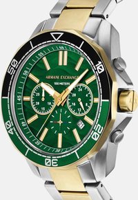 Žalias ciferblatas laikrodis su auksiniais ir sidabriniais metaliniais grandinėmis. Ypatybės apima tris subciferblatukus, datos rodmenį ir pažymėtą bezelį iki 100 metrų.