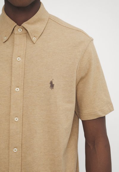 Camisa polo de manga curta bege com gola, apresenta um logótipo bordado tonal no peito e fechos de botão.