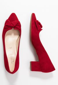 Chaussures à talons en velours rouge avec un bout pointu et un nœud décoratif à l'avant. Elles présentent un talon moyen épais et une doublure intérieure lisse.