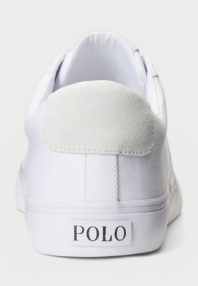 Vit kanvas sneaker med en texturerad mocka häldetalj, platt sula och en framträdande "POLO" logotyp på baksidan. Enkel, minimalistisk design.