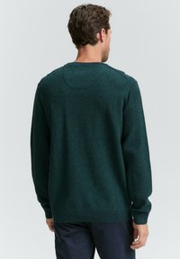 Pulover de culoare verde închis, cu un tricotaj texturat, manșete ribbate și un guler rotund. Design simplu, clasic, cu o croială lejeră.