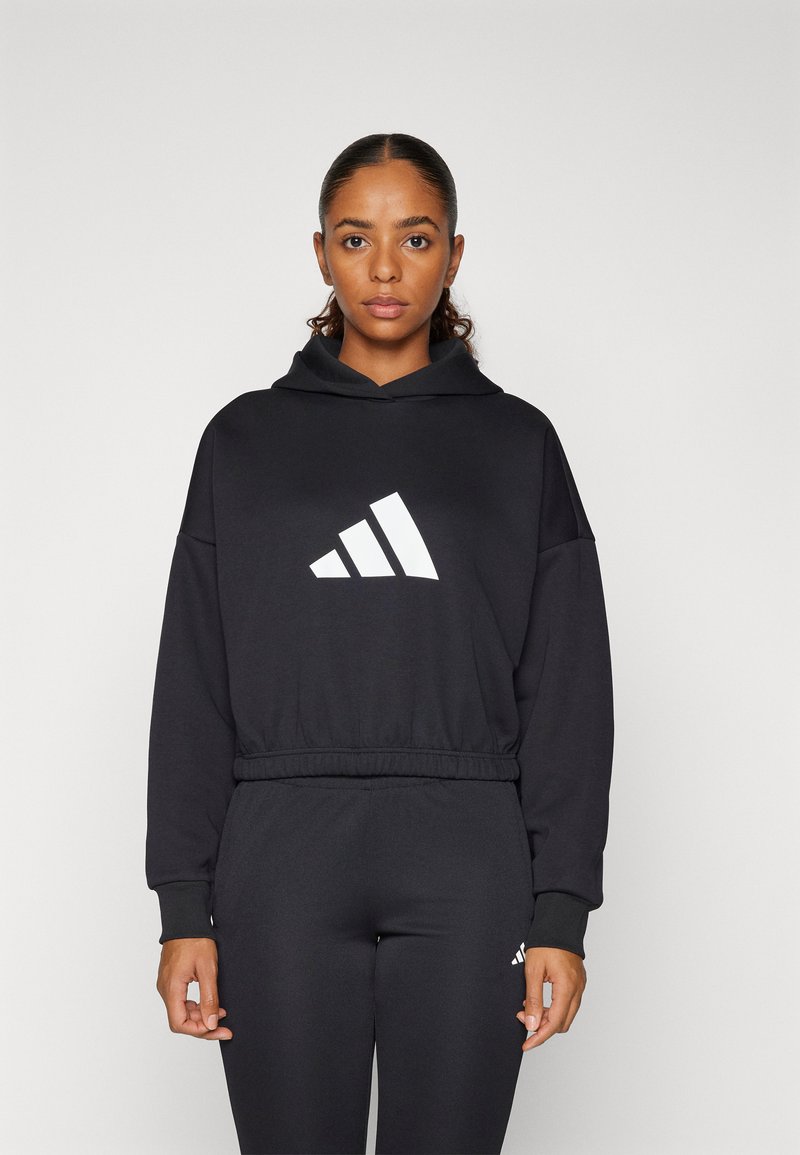 Juodas džemperis su dideliu balintu adidas logotipu priekyje, turintis kaklo raištelį, nėriniuotus rankogalius ir laisvą kirpimą.