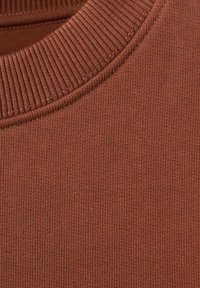 Ruskeaa ribbineulosta, jossa on pyöreä kaula-aukko; sileä pinta ja tasainen ompelu kaulan ympärillä.