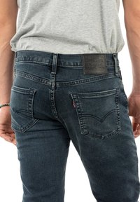 Jeans in denim blu scuro con vestibilità slim, caratterizzati da due tasche posteriori e un'etichetta in pelle sulla vita. Dettagli di cucitura minimalisti.