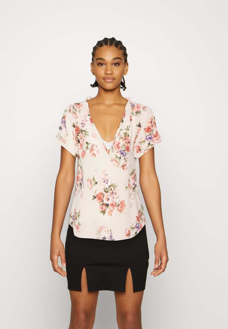 Top de estampado floral em tecido rosa claro com mangas curtas e decote em V profundo, combinado com uma saia preta com fendas laterais.