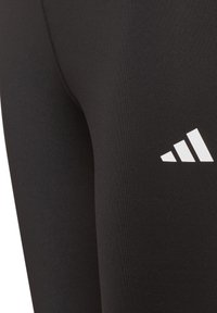 Leggings negros hechos de una tela suave, con un logo de Adidas de tres rayas blancas en la parte inferior de la pierna. Diseño atlético clásico, ajuste ceñido.