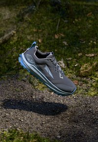 Graue Sportschuh mit blauen Akzenten; verfügt über eine abgerundete Zehenkappe, eine strukturierte Oberseite und eine ausgeprägte Sohle für besseren Grip. Leichtes Design, schwebender Effekt.
