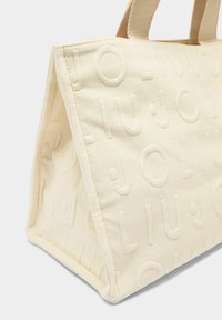 Roomkleurige draagtas met een reliëflogo-patroon, gemaakt van gestructureerd materiaal met stevige stoffen handvatten. Rechthoekige vorm.