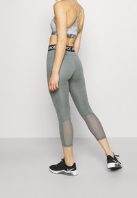 Leggings deportivos grises con paneles de malla, combinados con un sujetador deportivo gris. La cintura presenta un logo negro. Zapatillas deportivas negras completan el conjunto.