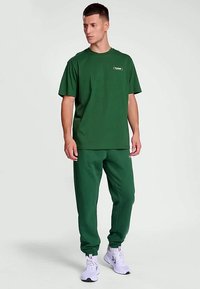 Zöld pamut póló kerek nyakkal, amelyet hozzá illő melegítőnadrággal párosítottak. Figyelemre méltó logó a pólón, szűkített nadrág és elasztikus mandzsetták.