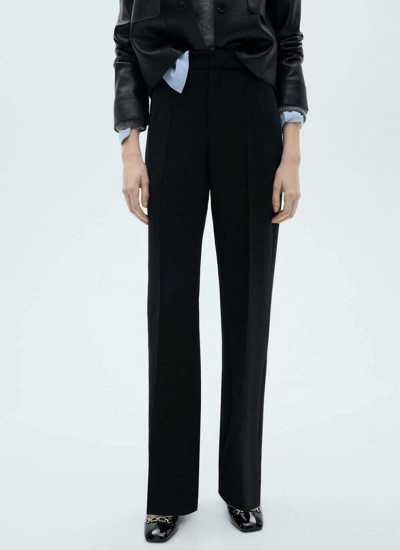Black tailored trousers, high-waisted with pleats, made of smooth material; paired with a fitted black jacket and shiny shoes.