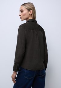 Donkergroene overhemd met lange mouwen en kraag, gemaakt van zachte stof. Heeft knoopmanchetten en een yoke-detail aan de achterkant.