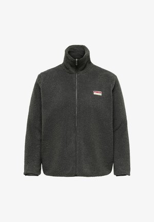 Kurtka z polaru w ciemnozielonym kolorze z wysokim kołnierzem i pełnym zamkiem z przodu. Na piersi małą naszywkę z logo marki. Miękki, teksturowany materiał.