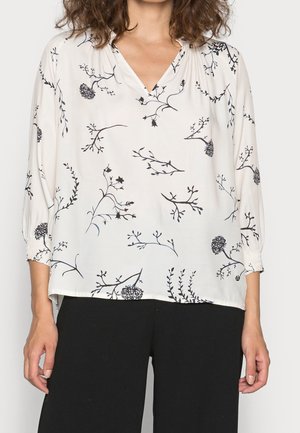 Weiße Bluse mit schwarzen Blumenmuster, V-Ausschnitt und Dreiviertelärmeln mit elastischen Bündchen. Hergestellt aus leichtem, glattem Stoff.