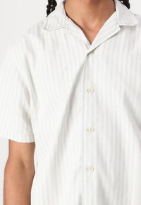 Chemise à manches courtes à boutons avec des rayures verticales bleu clair et blanches, en tissu doux, avec un col camp et des boutons clairs.