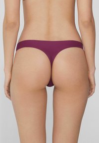 String en bourgogne avec une conception sans coutures, présentant une large ceinture et une texture lisse, mettant en avant une silhouette à couverture minimale.