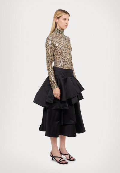 Top a collo alto in paillettes dorate con stampa leopardata, abbinato a una gonna a balze in satin nera. Strati dettagliati creano volume. Tacchi neri con cinturini.