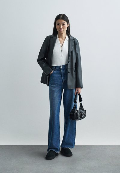 Czarna skórzana marynarka, prążkowany biały top z koronkowymi detalami, niebieskie dżinsy z wysokim stanem i dzwonami, czarna torebka z ćwiekami oraz czarne buty.