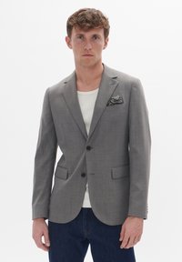 Šedý pruhovaný blazer s klopami, dvěma knoflíky a kapesníčkem v kontrastním vzoru. Má přiléhavý střih a dvě přední kapsy.