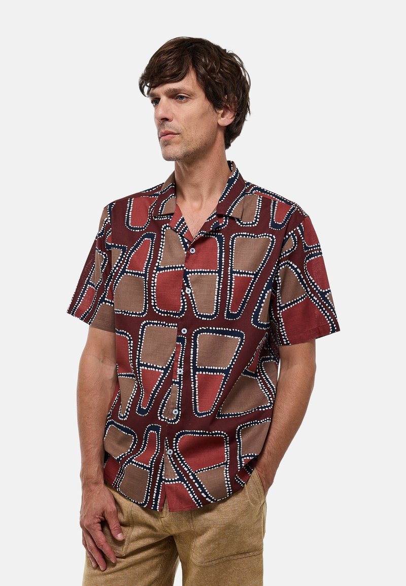 Chemise à manches courtes dans un motif géométrique rouge, marron et crème, avec des accents circulaires blancs et un col décontracté.