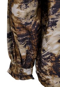 Tessuto di blusa marrone con motivi astratti neri e beige, caratterizzato da polsini arricciati e dettaglio dei bottoni. Texture liscia con una leggera lucentezza.