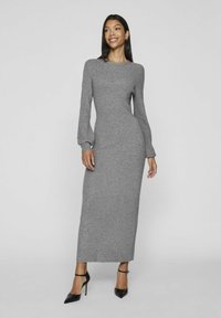 Abito maxi grigio a coste con maniche lunghe a sbuffo, scollatura rotonda e silhouette aderente, abbinato a tacchi neri a punta.