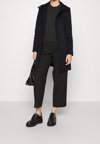 Laivastonsininen yllevaate, jossa on kaulus, käytetään tummanvihreän yläosan ja leveälahkeisten mustien housujen päällä. Mustat nauhakenkä ja pieni musta laukku korostavat asua.