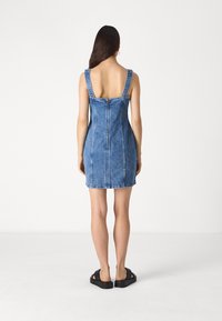 Rochie din denim cu o siluetă ajustată, decolteu pătrat, bretele late și închidere cu fermoar la spate. Prezintă o nuanță de albastru estompat și detalii cusute.