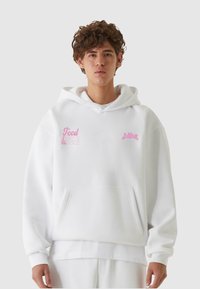 Hvit hettegenser med en frontlomme, som har rosa brodert tekst "Mat & Venner" og "Sublime" på brystet. Myk stofftekstur.