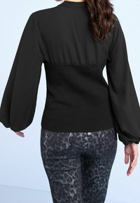 Blouse noire avec de longues manches bouffantes et une taille ajustée côtelée, associée à un jean à imprimé léopard foncé avec cinq poches et un léger brillant.