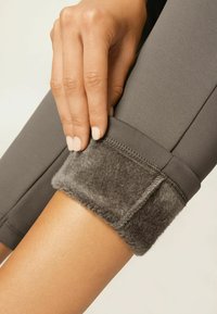 Poignet de legging gris avec une douce doublure en peluche grise. Une main tient le poignet pour mettre en valeur la texture et le détail du design. Tissu lisse sur la jambe.