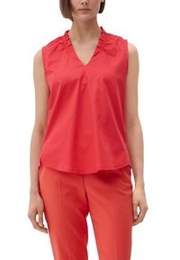Blusa roja sin mangas con escote en V, detalle fruncido en el cuello y tela suave. Llevada con pantalones rojos a juego.