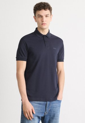 Polo shirt bleumarin din bumbac, cu un clapetă cu două butoane și mâneci scurte. Detaliu logo discret pe pieptul stâng. Design ajustat.