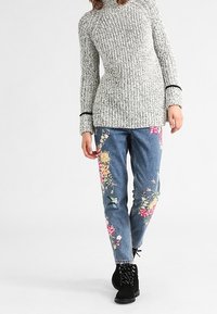 Grå stickad tröja med svarta detaljer, ihop med blåjeans med färgglad blommönstring på benen, bärs med svarta snörskor.
