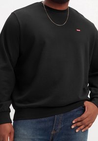 Felpa nera con maniche lunghe, collo a giro e orlo a costine. Presenta un piccolo logo rosso di Levi's sul petto. Jeans in denim scuro.