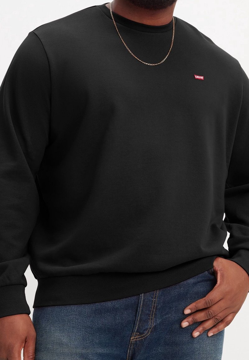 Felpa nera con maniche lunghe, collo a giro e orlo a costine. Presenta un piccolo logo rosso di Levi's sul petto. Jeans in denim scuro.