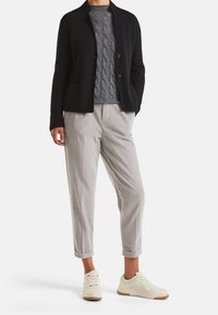 Černá, zapínací bunda s límcem, položená na texturovaném šedém svetru. Světle šedé, skládací kalhoty a bílé tenisky s gumovými podrážkami.