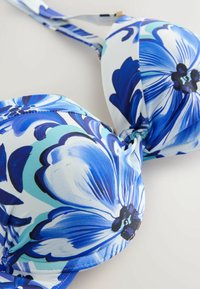 Top de bikini imprimat cu flori albastre și albe, cu cupe modelate, bretele reglabile și detaliu cu nod central. Prezintă accente de albastru închis.