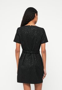 Μαύρο φόρεμα με κοντά μανίκια, υφασμάτιν�η υφή, τονισμένη μέση και φερμοάρ στην πλάτη. Μήκος πάνω από το γόνατο με λεπτό μοτίβο σε όλη την επιφάνεια.