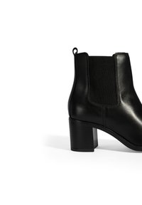 Botte cheville en cuir noir avec un panneau latéral élastique, bout rond et un talon carré texturé. Dispose d'une languette pour un enfilage facile.