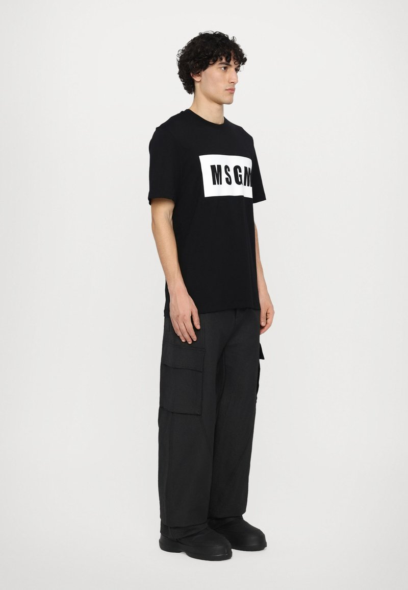 Schwarzes T-Shirt mit weißem "MSGM"-Logo auf der Vorderseite, kombiniert mit lockeren schwarzen Cargo-Hosen mit mehreren Taschen.