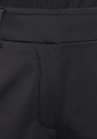 Tela negra y suave de pantalones con una pretina plana, costura lateral y un bolsillo discreto. La costura es visible a lo largo de los bordes.