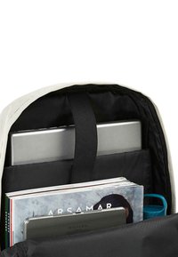 Interior de mochila de lona clara con un forro negro, que contiene una laptop plateada, revistas y una botella de agua azul.