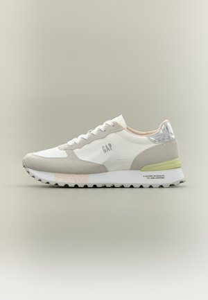 Bílá a béžová volnočasová teniska se šedou podrážkou, stříbrným ozdobným prvkem na patě, logem „GAP“ na boku a vzorkovanou podrážkou na neutrálním pozadí.