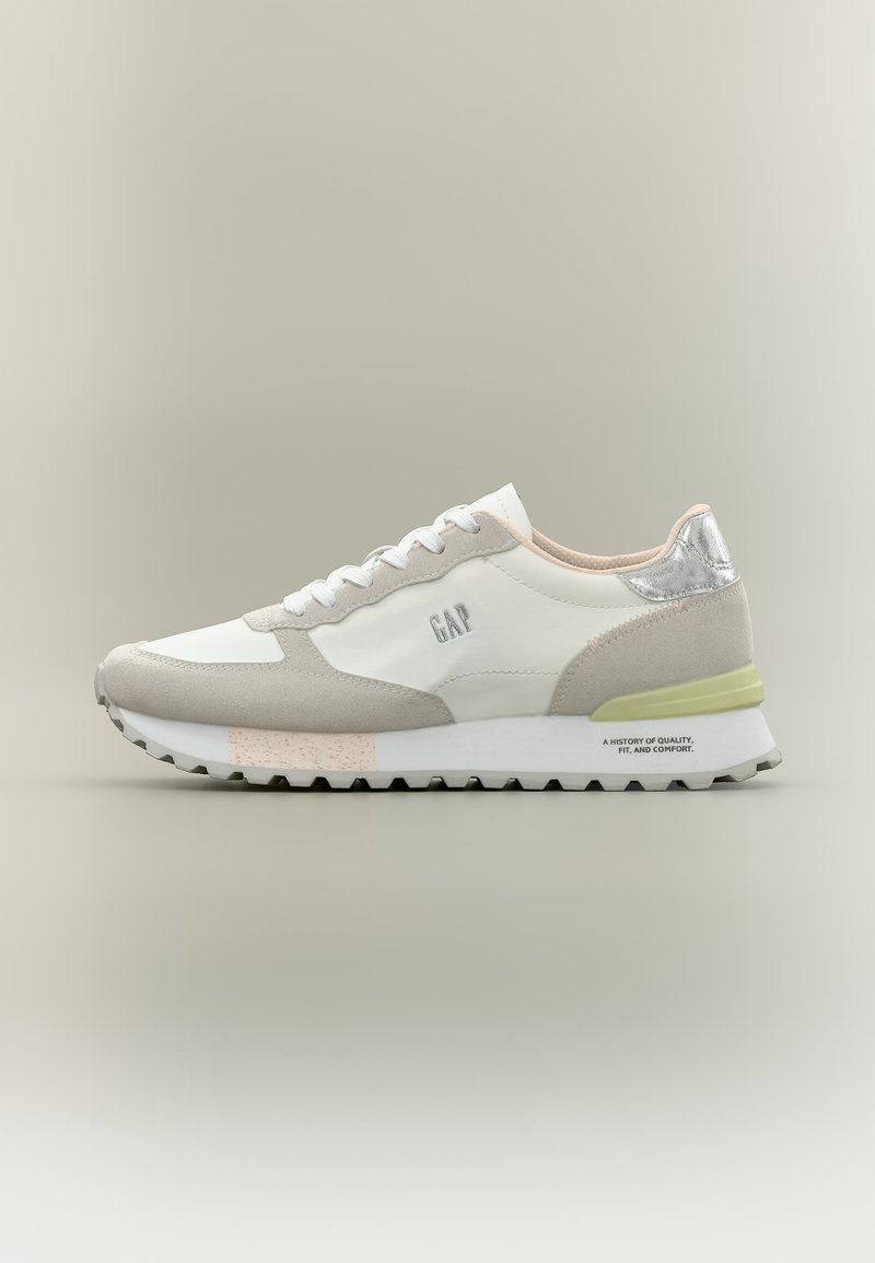 Baskets décontractées blanches et beiges avec une semelle grise, un accent talon argenté, le logo "GAP" sur le côté et une semelle extérieure rainurée sur un fond neutre.