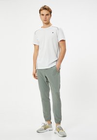 Witte kortemouw t-shirt met ronde hals en blauwe stiksels, gecombineerd met lichtgroene joggingsbroek met zakken en een smalle pasvorm.